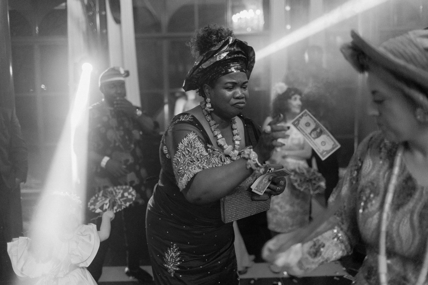 A woman in traditional attire holds cash at a lively event with others in the background.