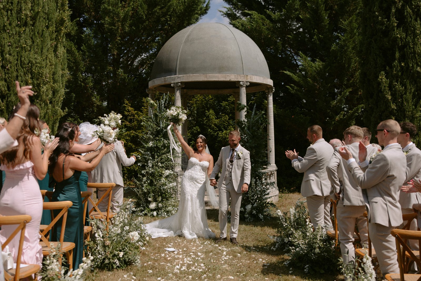 A newlywed couple walks down the aisle under a gazebo, holding hands and celebrating. Guests in formal attire applaud and cheer them on. Chateau la Durantie Wedding Photographer.
