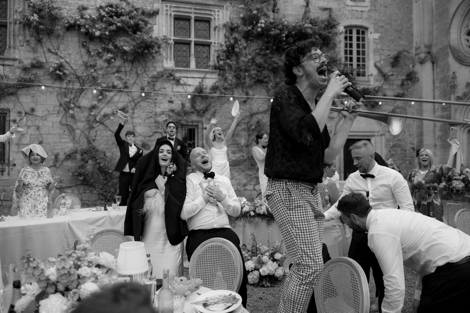A singer performs energetically on a table at an outdoor wedding reception as guests cheer and celebrate around him.