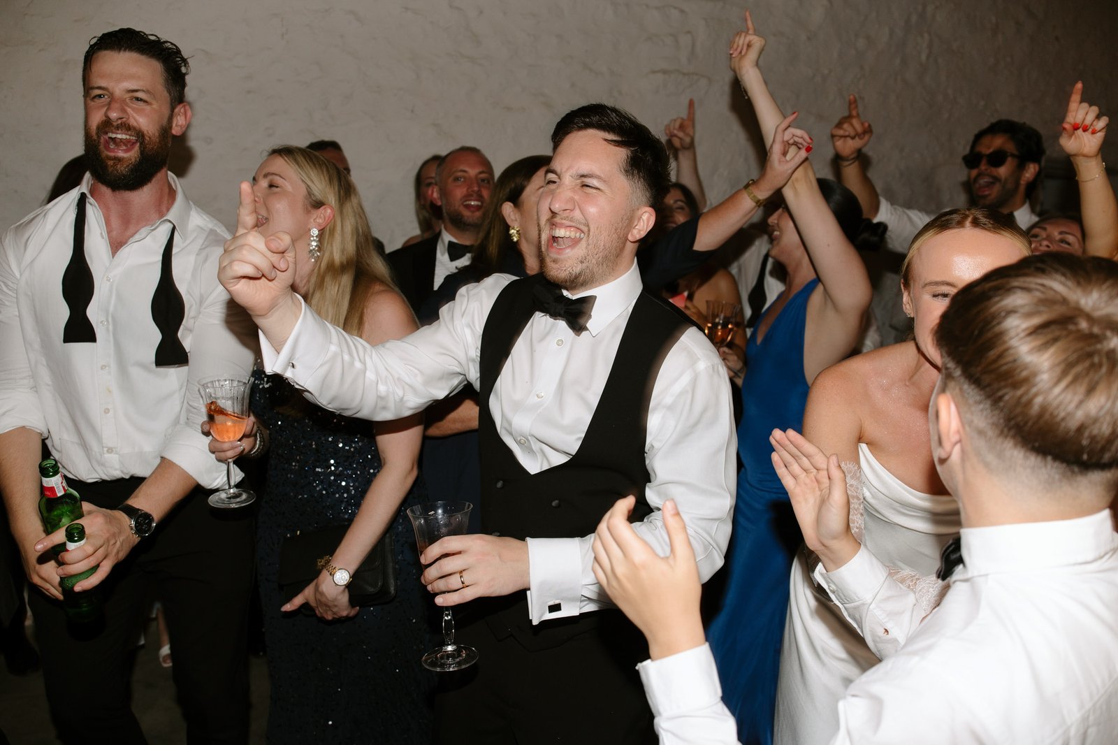 A group of people in formal attire laugh, cheer, and raise their hands while celebrating at an indoor event.