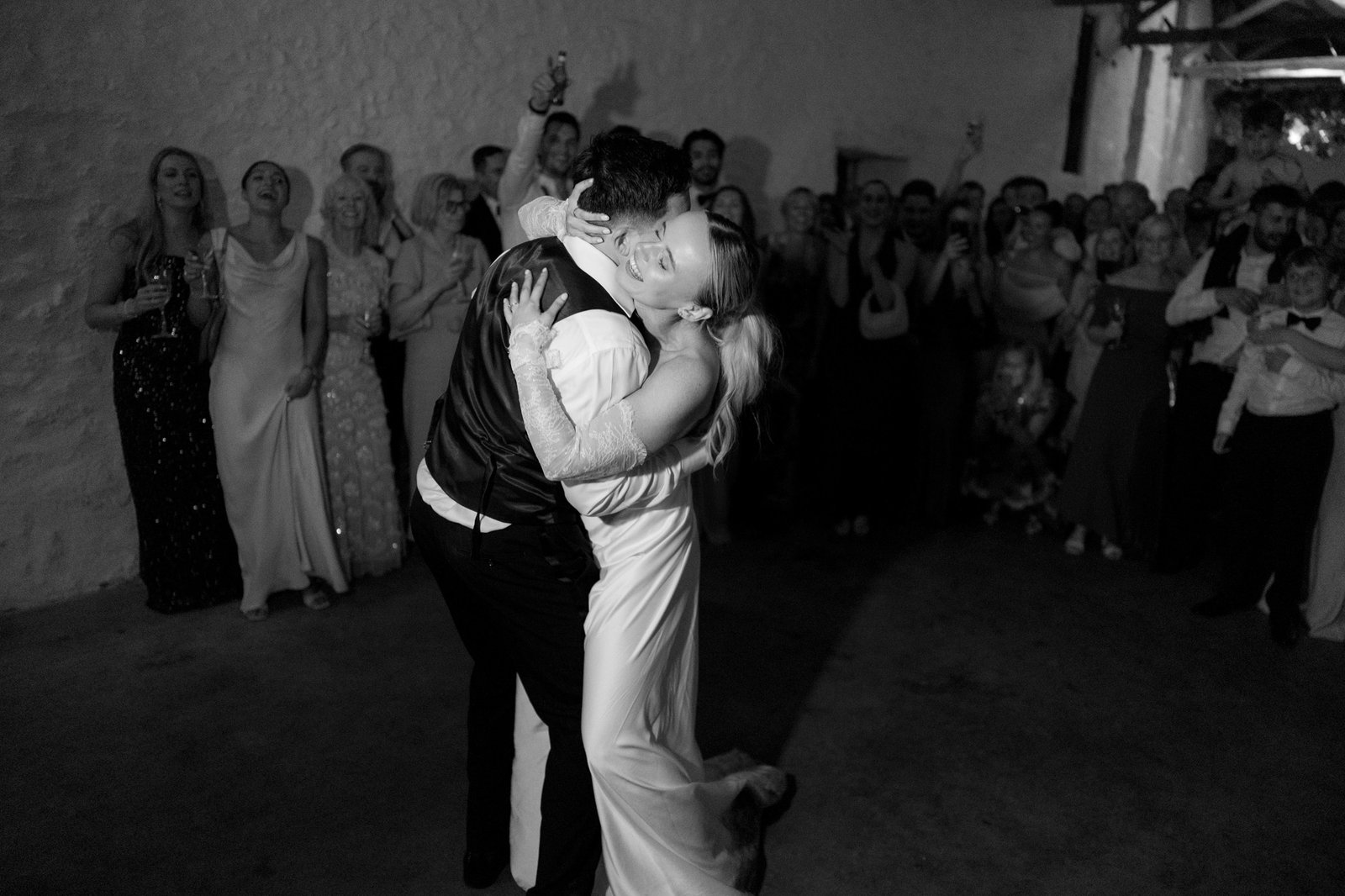 A couple embraces and dances in the center of a room while a group of people stands around them, watching and celebrating.