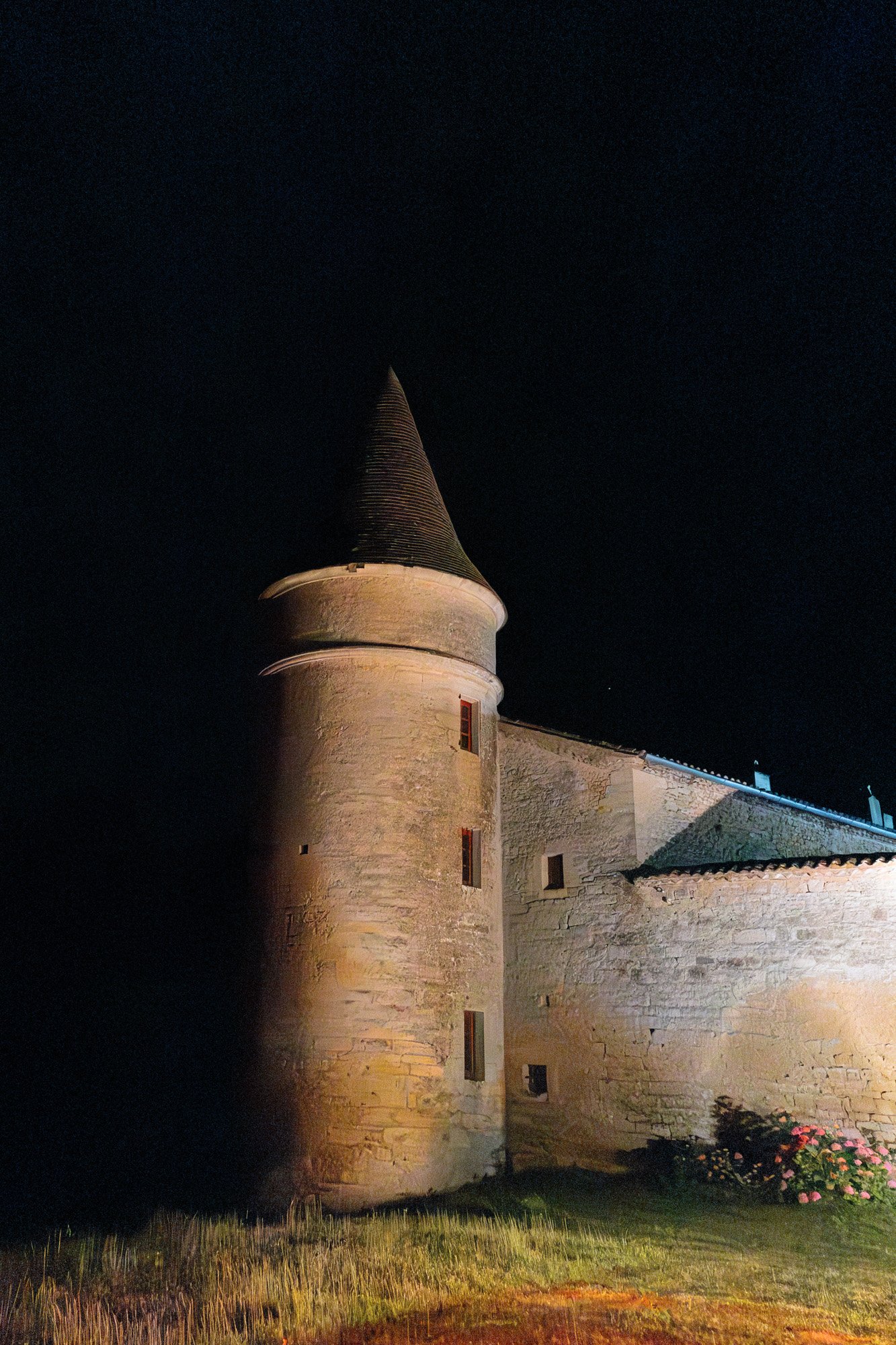 A stone building with a pointed roof at night. Chateau de la Bourlie wedding.