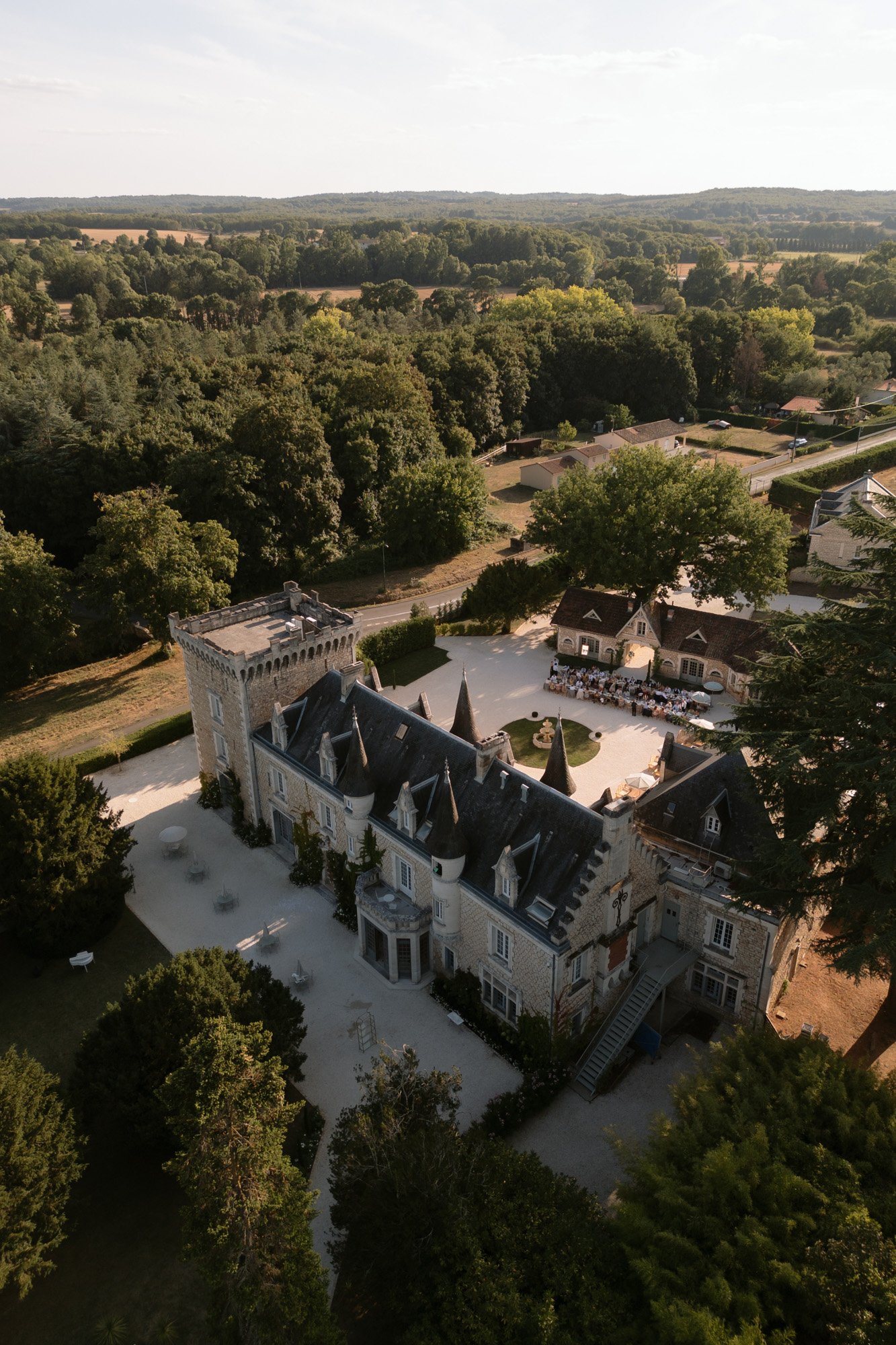 Aerial view of a large stone chateau with pointed roofs, surrounded by trees and greenery, located in a rural landscape. Chateau de la Couronne wedding.