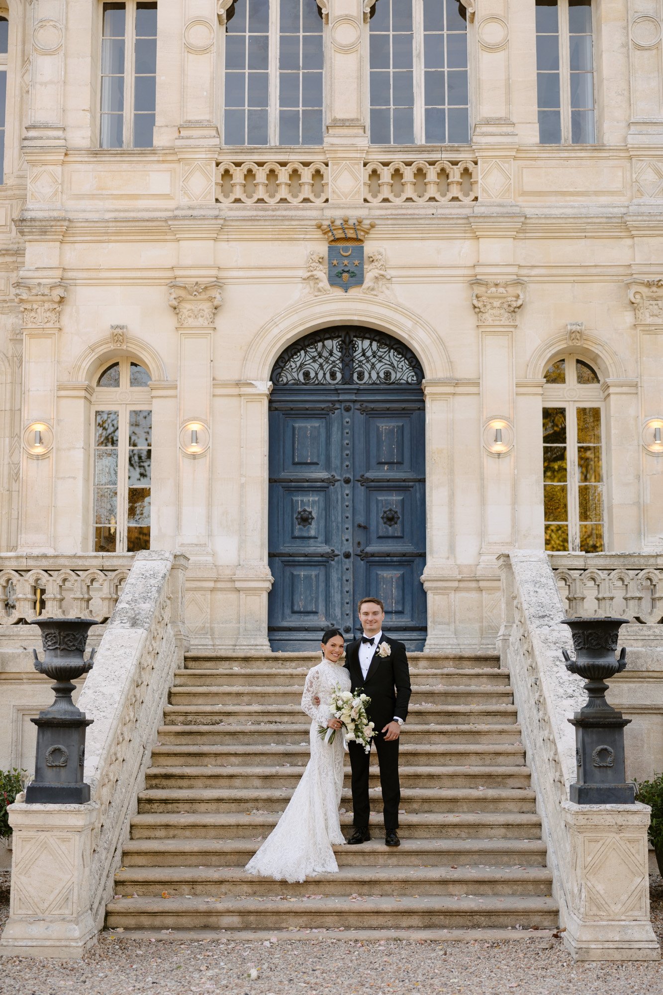 A man and woman standing on stairs in front of a building. Chateau de la Valouze wedding.
