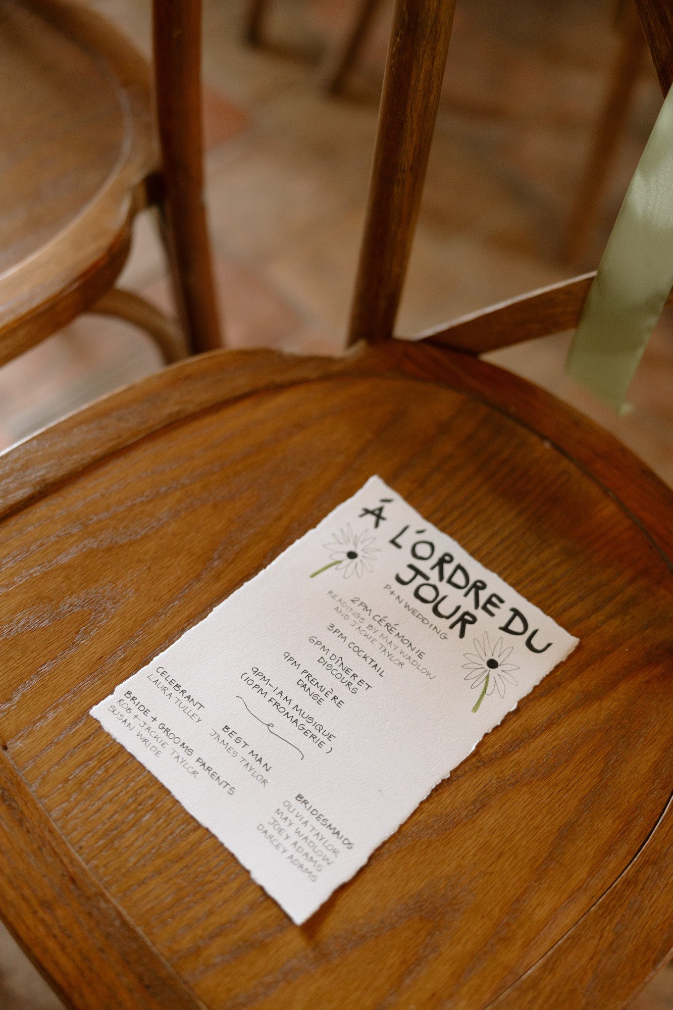 A printed paper with the heading A LORDRE DU JOUR and a list of event details rests on a wooden chair.