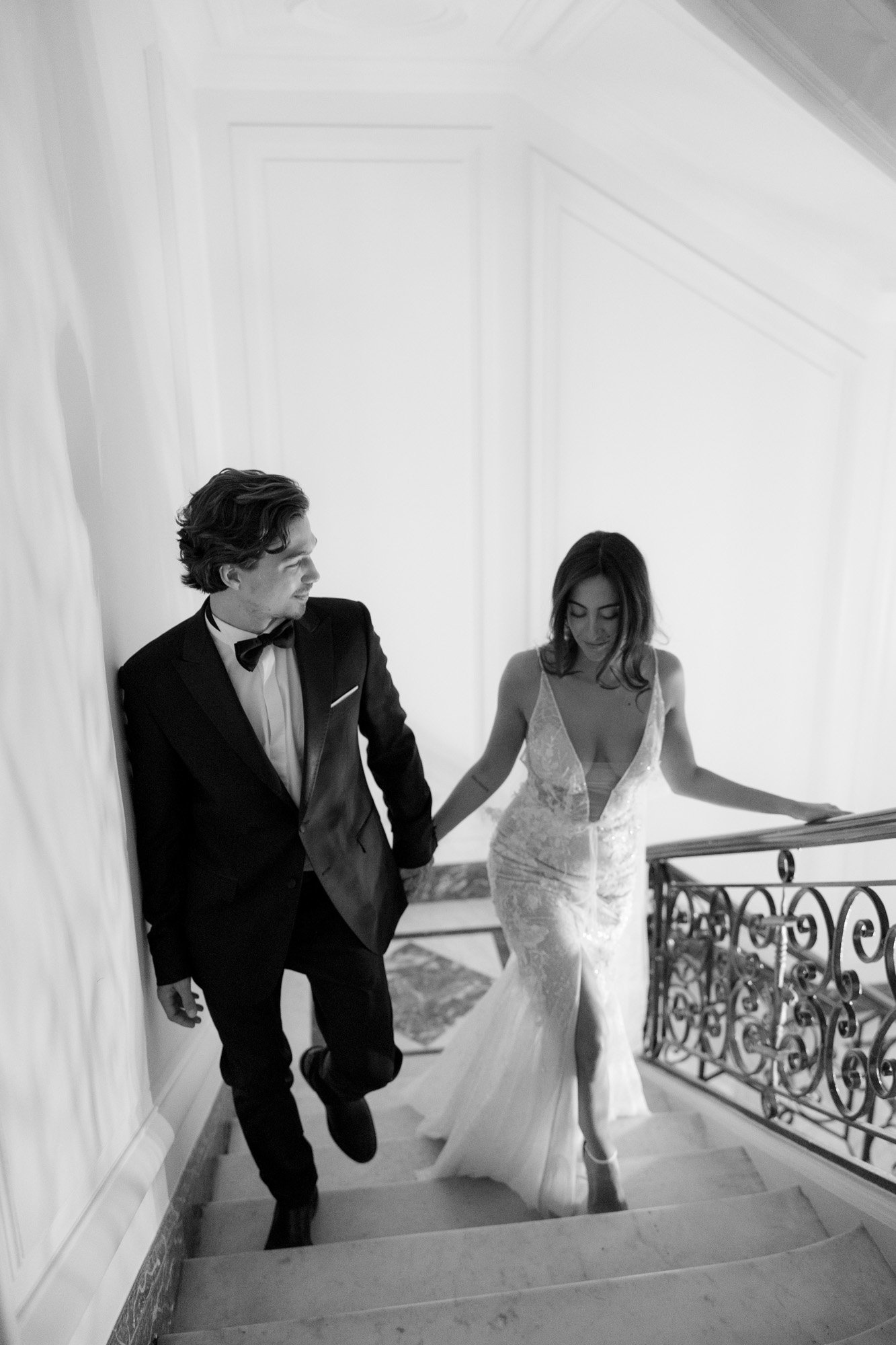 A man in a tuxedo and a woman in a wedding dress walk up a staircase, holding hands. Hotel Alfred Sommier Elopement.